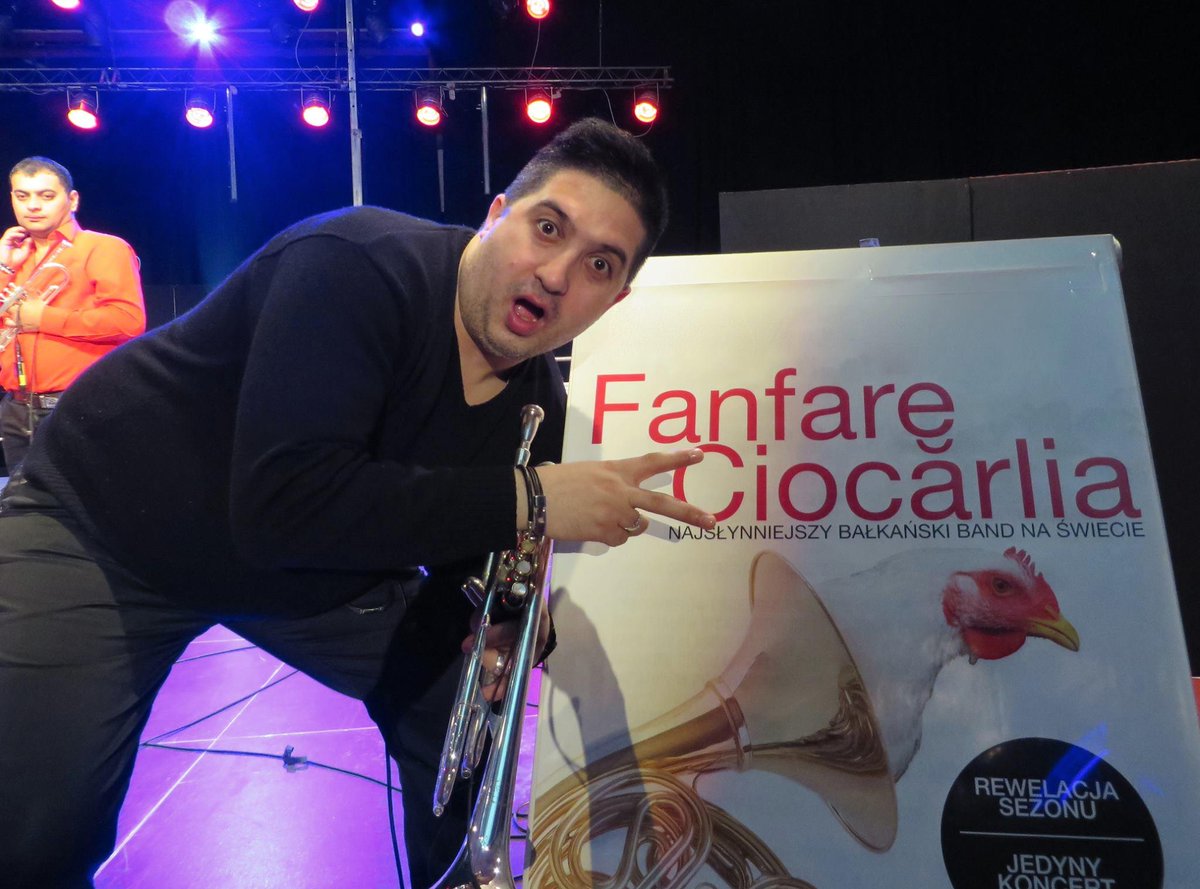 Trumpeter Marian giving a peace sign to a Fanfare Ciocarlia poster of a rooster hanging out of a horn