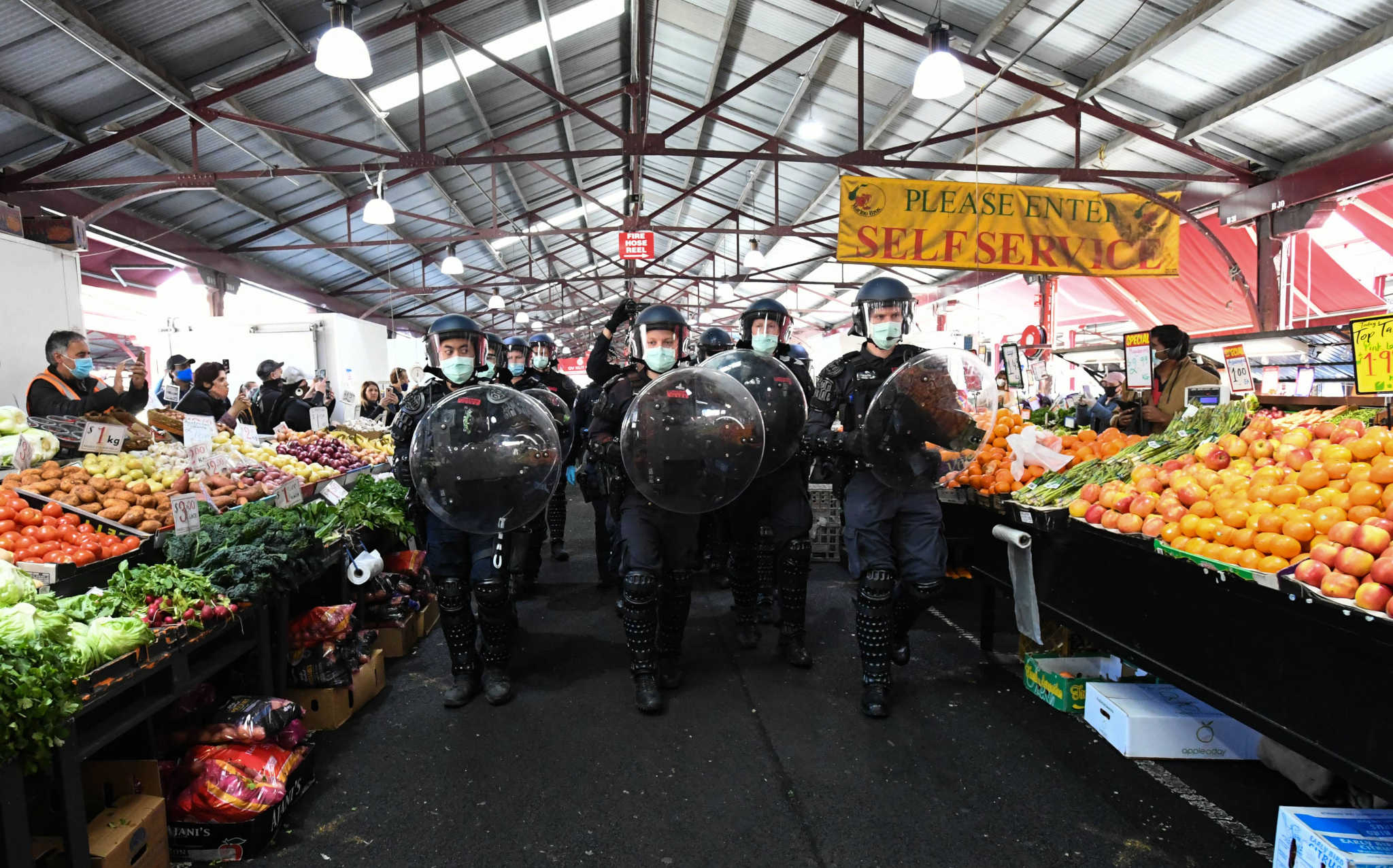 Crowd control officers in formation and with full regalia walking through the Queen Victoria Market with fruit and vegetable stalls on either side of them